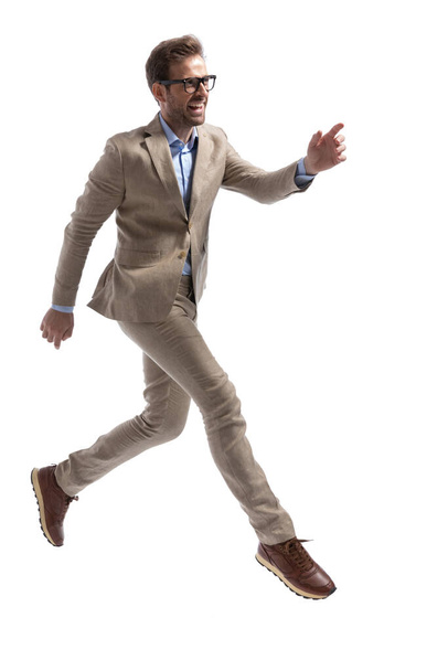 joven hombre de negocios corriendo para atrapar algo, sonriendo y usando anteojos sobre fondo blanco - Foto, Imagen