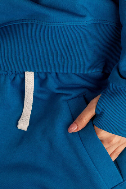 Gros plan de la main d'une fille dans une poche de sweat-shirt. Fragment d'une photographie d'une femme portant un sweat sport. Publicité pour vêtements de sport à la mode. Couleur bleue - Photo, image