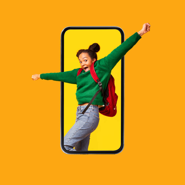 Podekscytowana czarna nastolatka krzyczy na ekranie telefonu komórkowego, pomarańczowe tło - Zdjęcie, obraz