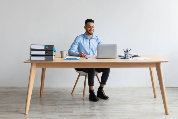 Arab muž pomocí notebooku sedí za stolem v kanceláři - Fotografie, Obrázek