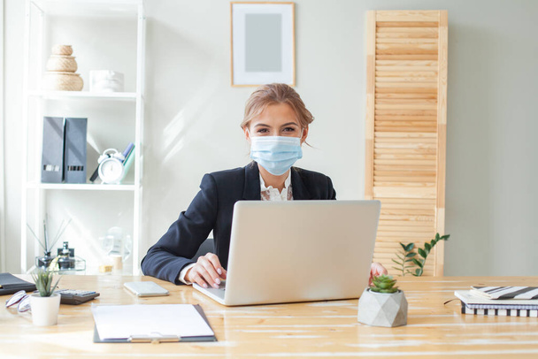 Executive woman working at her desk and wearing a protective mask against covid-19 - Fotó, kép