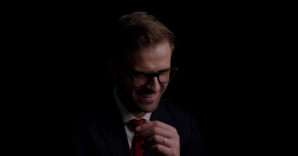 молодой привлекательный бизнесмен чешет подбородок, носит очки и смотрит в сторону на темном фоне - Кадры, видео