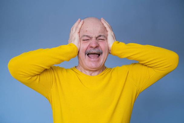 Senior man bedekt zijn oren met geheven handpalmen met vreselijke hoofdpijn. - Foto, afbeelding