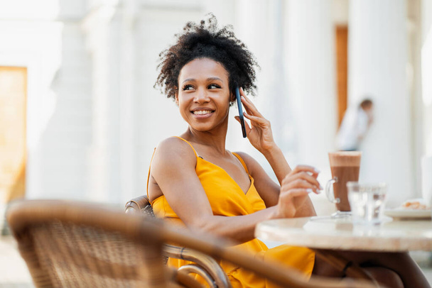A woman smiles at an Afro-looking student chatting on the phone with friends. A freelancer uses a gadget. - Foto, afbeelding