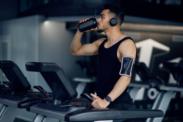 Arab Guy Drinking Protein Cocktail From Sport Shaker While Training On Treadmill - Photo, Image