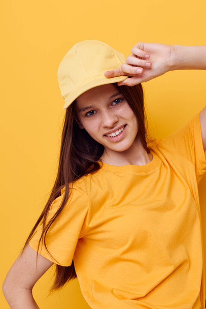 young beautiful woman posing in a yellow T-shirt and cap yellow background - Фото, зображення