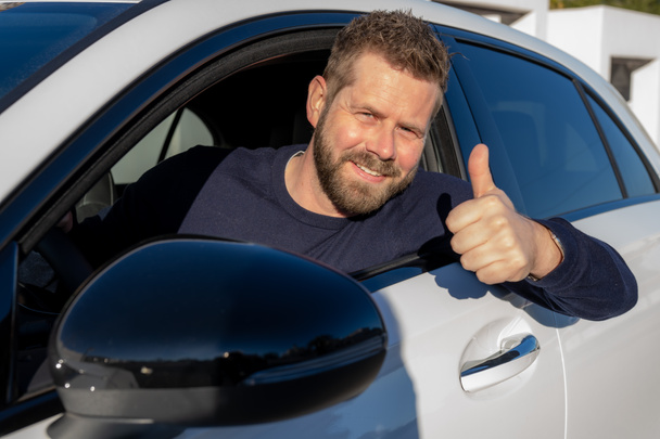 Young smiling man doing thumps-up in car - Photo, image