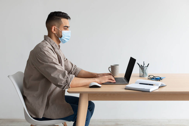 Uomo in maschera protettiva che lavora su pc in home office - Foto, immagini