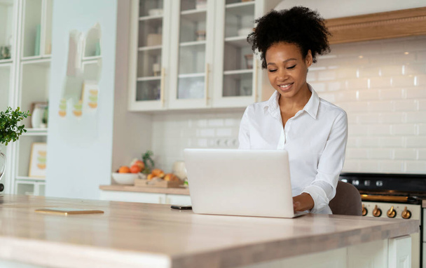 Student at home online learning. A woman surfing the internet. The blogger is working on a laptop. Workplace in the kitchen. A freelancer prints a message to clients on a social network. - Photo, Image