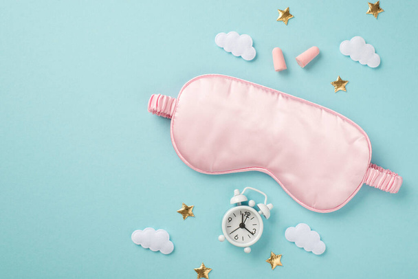 Top view photo of pink satin sleeping mask alarm clock earplugs clouds and golden stars on isolated pastel blue background with copyspace - 写真・画像