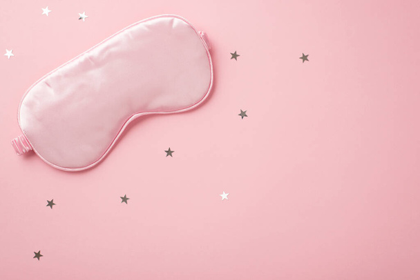 Top view photo of pink silk sleeping mask and star shaped confetti on isolated pastel pink background with copyspace - Fotoğraf, Görsel
