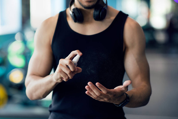 Hombre muscular irreconocible aplicando aerosol desinfectante en las manos antes de entrenar en el gimnasio - Foto, Imagen
