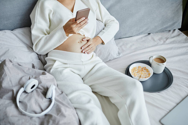 Terhes nő mobiltelefont használ az ágyban - Fotó, kép