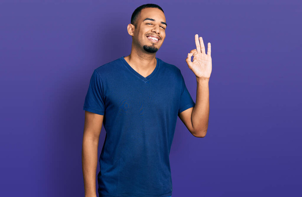 Giovane uomo afroamericano indossa maglietta casual sorridente positivo facendo ok segno con le mani e le dita. espressione di successo.  - Foto, immagini