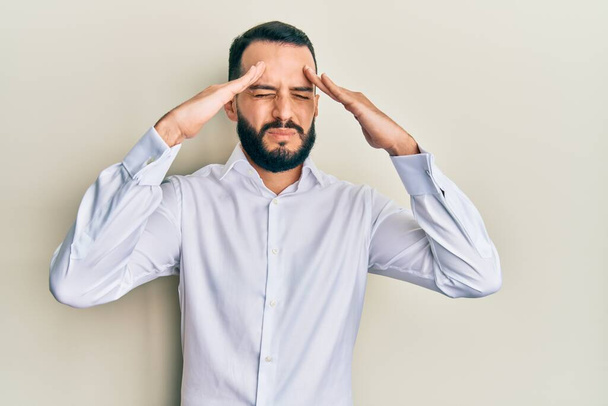 Hombre joven con barba llevando camisa blanca de negocios con la mano en la cabeza, dolor de cabeza porque el estrés. padecer migraña.  - Foto, imagen