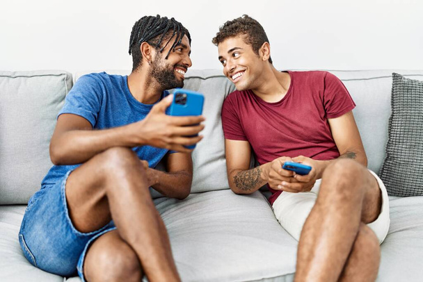 Two men friends using smartphone sitting on sofa at home - Fotó, kép