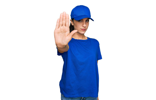 Young hispanic girl wearing delivery courier uniform doing stop sing with palm of the hand. warning expression with negative and serious gesture on the face.  - Photo, Image