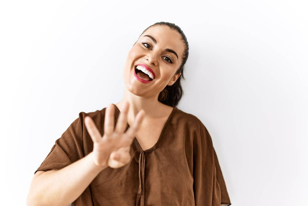 Young brunette woman standing over isolated background showing and pointing up with fingers number four while smiling confident and happy.  - Photo, Image