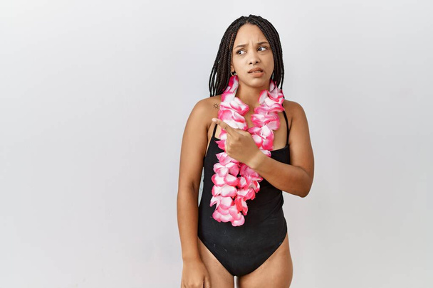 Mladá africká Američanka v plavkách a havajském lei ukazuje stranou ustaraný a nervózní ukazováčkem, ustaraný a překvapený výraz  - Fotografie, Obrázek