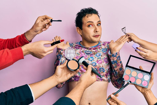 Handsome man wearing make up with make up cosmetics around clueless and confused with open arms, no idea and doubtful face.  - Photo, Image