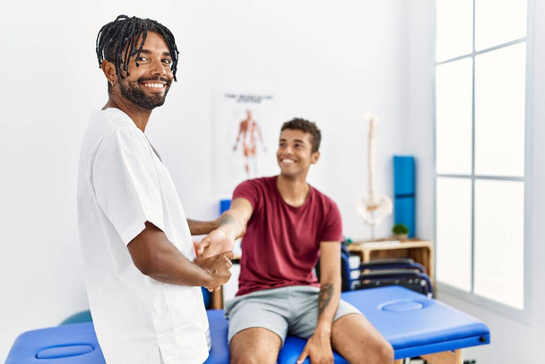 Dois homens fisioterapeuta e paciente tendo braço de alongamento sessão de reabilitação na clínica - Foto, Imagem