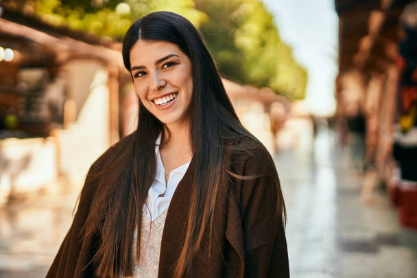 若いヒスパニック系の女性が幸せそうに街に立って笑っている. - 写真・画像
