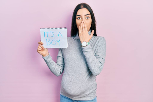 Beautiful woman with blue eyes expecting a baby holding its a boy banner covering mouth with hand, shocked and afraid for mistake. surprised expression  - Zdjęcie, obraz