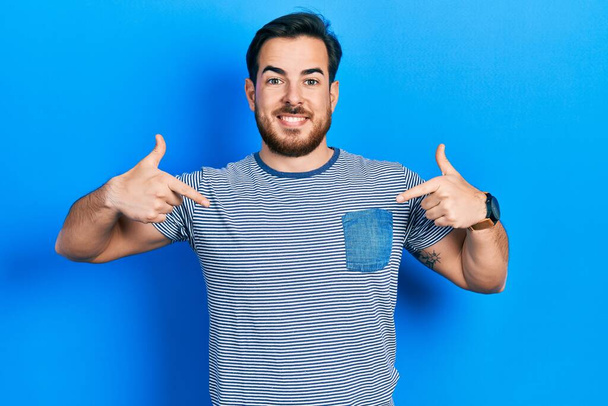 bel homme caucasien avec barbe portant casual t-shirt rayé regardant confiant avec sourire sur le visage, se pointant avec les doigts fiers et heureux.  - Photo, image