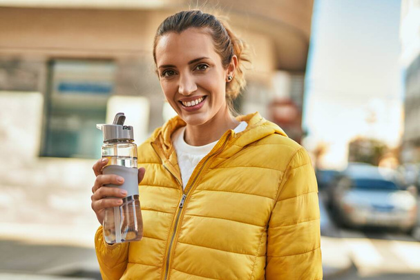 Молодая латиноамериканка улыбается счастливой питьевой бутылке воды в городе. - Фото, изображение
