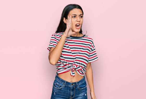 Young hispanic girl wearing casual clothes shouting and screaming loud to side with hand on mouth. communication concept.  - Photo, Image