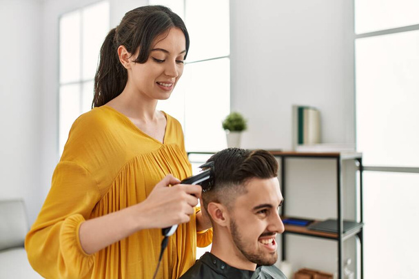 Mladý hispánský kadeřník žena řezání vlasů muže pomocí elektrického holicí strojek v centru krásy. - Fotografie, Obrázek