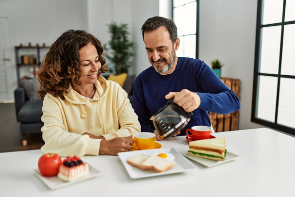 Middle age hispanic couple smiling happy sitting on the table having breakfast at home. - Foto, immagini