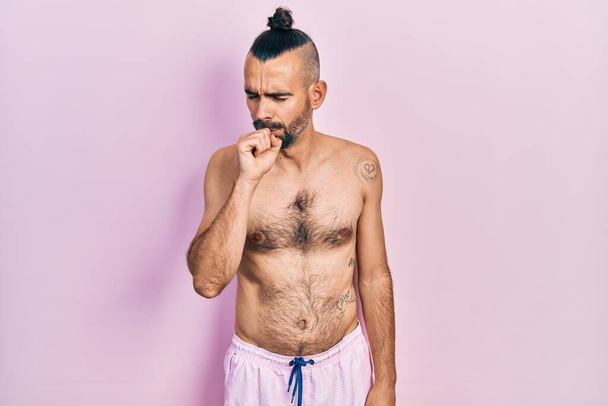 Joven hombre hispano sin camisa usando traje de baño sintiéndose mal y tosiendo como síntoma de resfriado o bronquitis. concepto de atención sanitaria.  - Foto, imagen