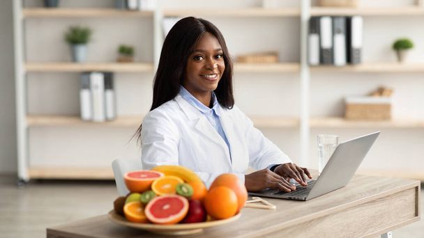 Concepto de nutrición saludable. consultor de pérdida de peso afroamericano escribiendo en el ordenador portátil, dando consulta en línea - Foto, imagen