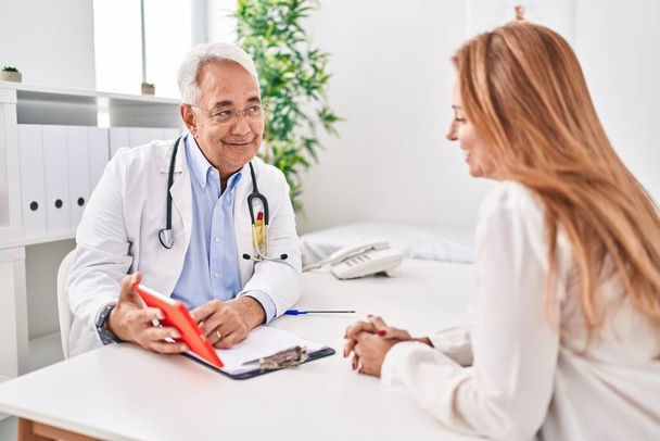 Middelbare leeftijd man en vrouw arts en patiënt met behulp van touchpad met medische consultatie in de kliniek - Foto, afbeelding