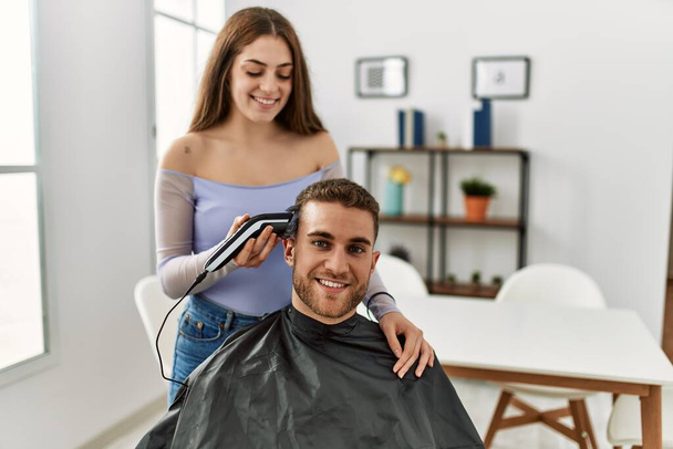 Young woman cutting hair her boyfriend at home. - Photo, image