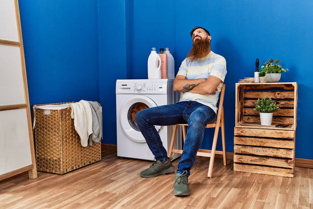 Fiatal vörös férfi fáradt vár mosógép a mosókonyhában - Fotó, kép