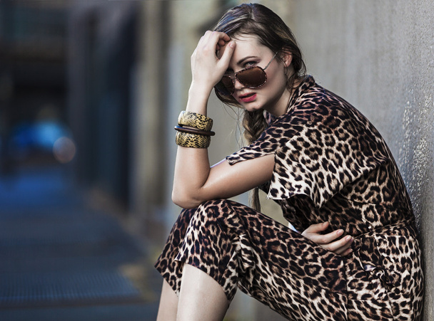 Mujer débil sentada en la ciudad y con un vestido de piel de leopardo
 - Foto, imagen