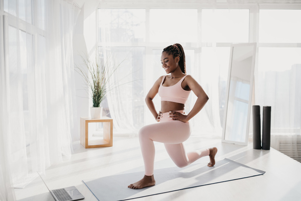 Молода чорна жінка робить лаунж, робить силові вправи, працюючи в онлайн-спортивному підручнику вдома, порожній простір
 - Фото, зображення