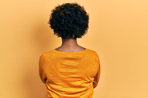 Junge Afroamerikanerin in lässiger Kleidung steht rückwärts und blickt mit verschränkten Armen weg  - Foto, Bild