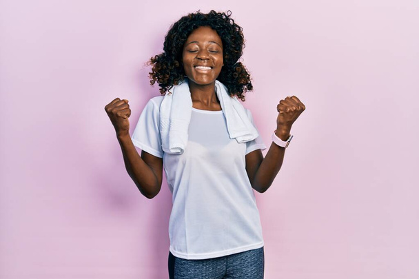 Mujer afroamericana joven con ropa deportiva y toalla muy feliz y emocionada haciendo gesto ganador con los brazos levantados, sonriendo y gritando por el éxito. concepto de celebración.  - Foto, Imagen