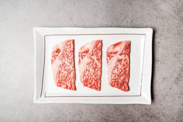 Top view of premium rare slices sirloin Wagyu A5 beef with high-marbling texture on a ceramic plate, Served for Yakiniku, Sukiyaki and Shabu. Image with copy space. - Fotografie, Obrázek