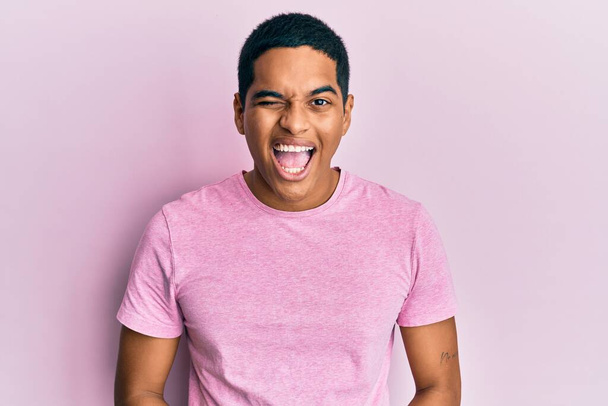 Fiatal jóképű spanyol férfi visel alkalmi rózsaszín póló kacsintás a kamerába szexi kifejezés, vidám és boldog arc.  - Fotó, kép