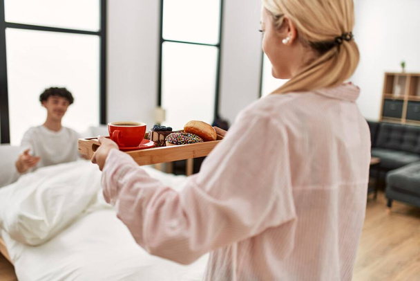 Kobieta zaskakująca swojego chłopaka śniadaniem na łóżku w domu. - Zdjęcie, obraz