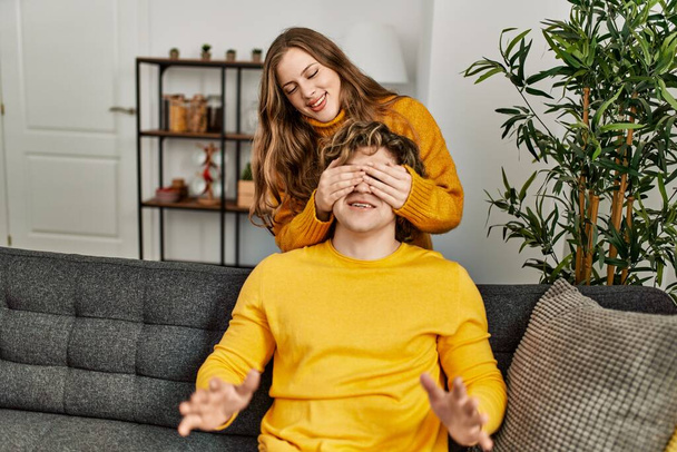 Young caucasian couple smiling confident surprise with hands on eyes at home - 写真・画像