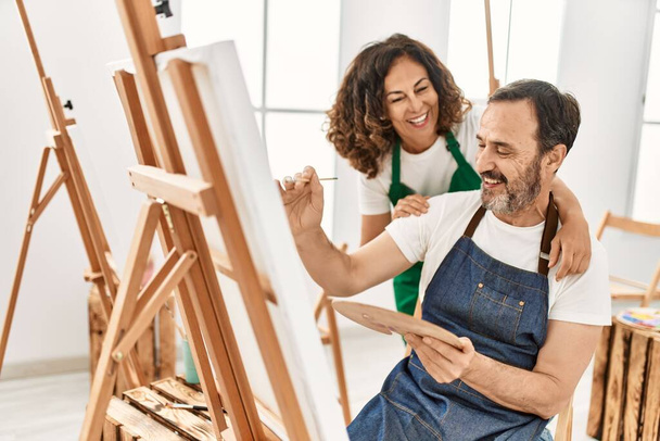 Estudiante de mediana edad y profesor sonriendo feliz pintura en la escuela de arte. - Foto, Imagen
