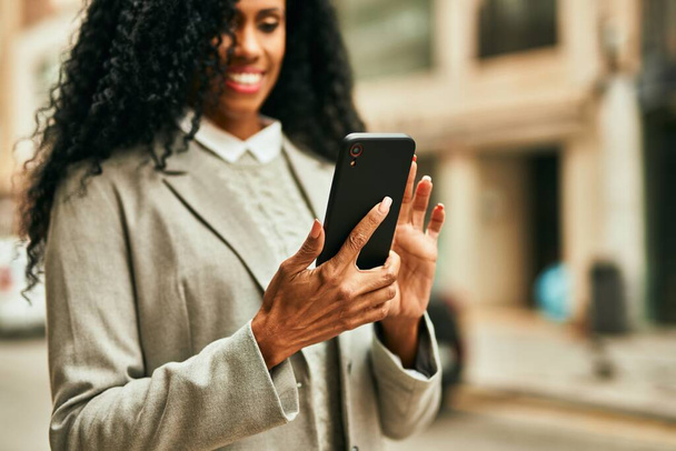 Middelbare leeftijd Afrikaanse Amerikaanse zakenvrouw met behulp van smartphone in de stad. - Foto, afbeelding