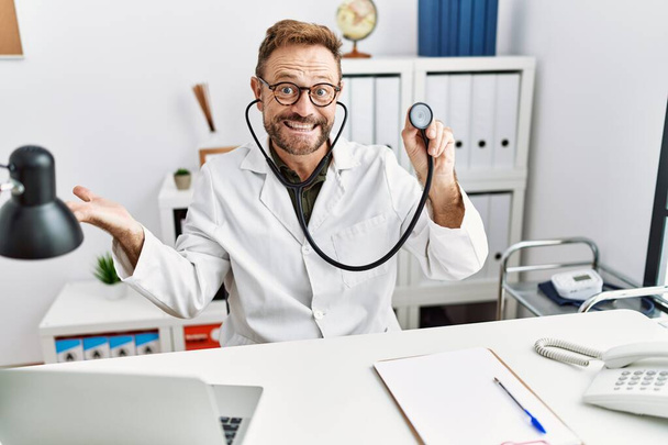 Uomo di mezza età con barba indossando uniforme medico tenuta stetoscopio celebrando il raggiungimento con sorriso felice e l'espressione del vincitore con mano alzata  - Foto, immagini