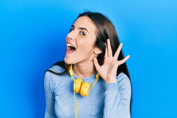 Fiatal barna tinédzser fülhallgatót visel a nyakán mosolyogva, fültől fülig hallgatva és hallva pletykákat vagy pletykákat. süketség fogalma.  - Fotó, kép