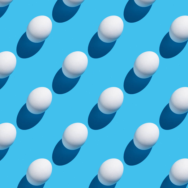 Il motivo delle loro uova bianche con un'ombra dura su uno sfondo blu. Sfondo minimalista astratto Pasqua. - Foto, immagini